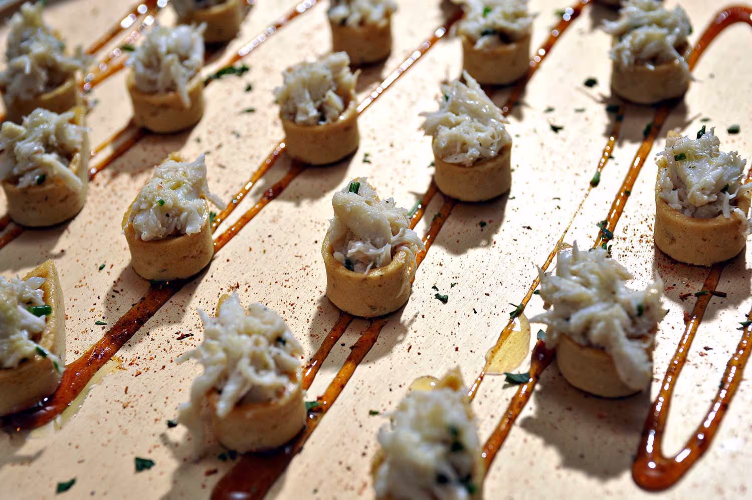 Rows of small round appetizers topped with shredded crab meat on a surface drizzled with a dark sauce.