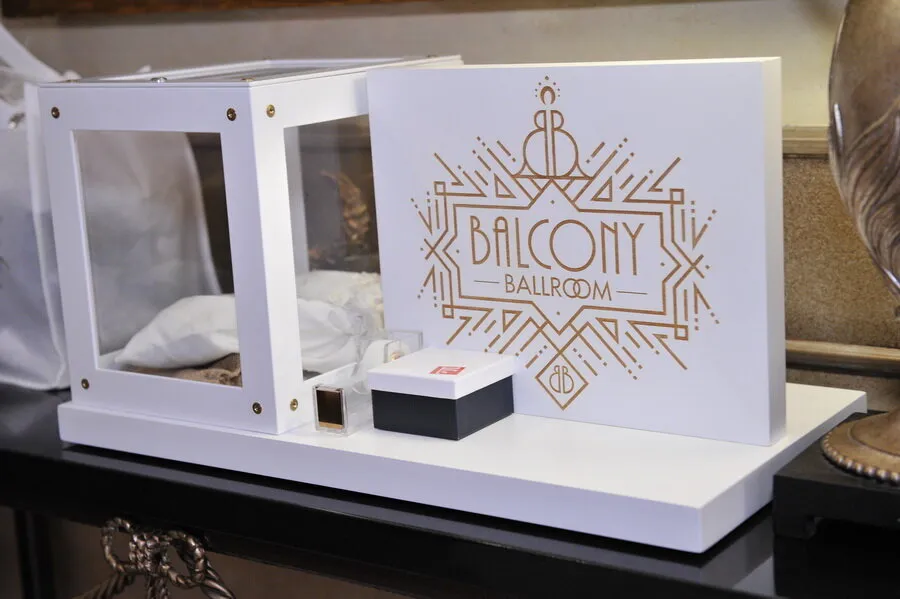 White display box with transparent sides, small black and white box, and a sign reading 'Balcony Ballroom' in gold decorative lettering on a white stand.