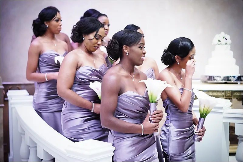 Bridesmaids in matching lavender dresses holding white calla lilies, with one wiping her eyes.