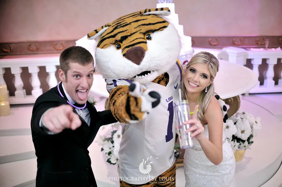 Bride and groom posing happily with LSU tiger mascot at wedding reception.