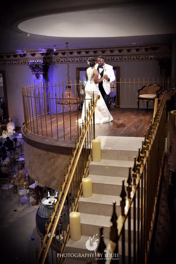 Bride and groom dancing on an elevated wooden platform with gold railings and white candles on the staircase in a decorated wedding venue.
