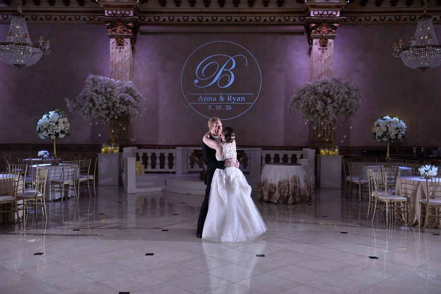Bride in white dress with long train descending an indoor staircase with golden railings, smiling and holding the rail.