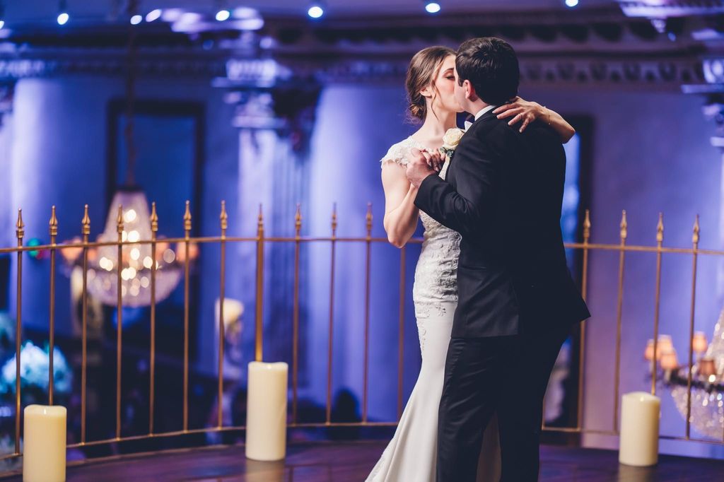 Bride in white wedding dress holding a bouquet with blue and white flowers standing in front of a decorated fireplace.
