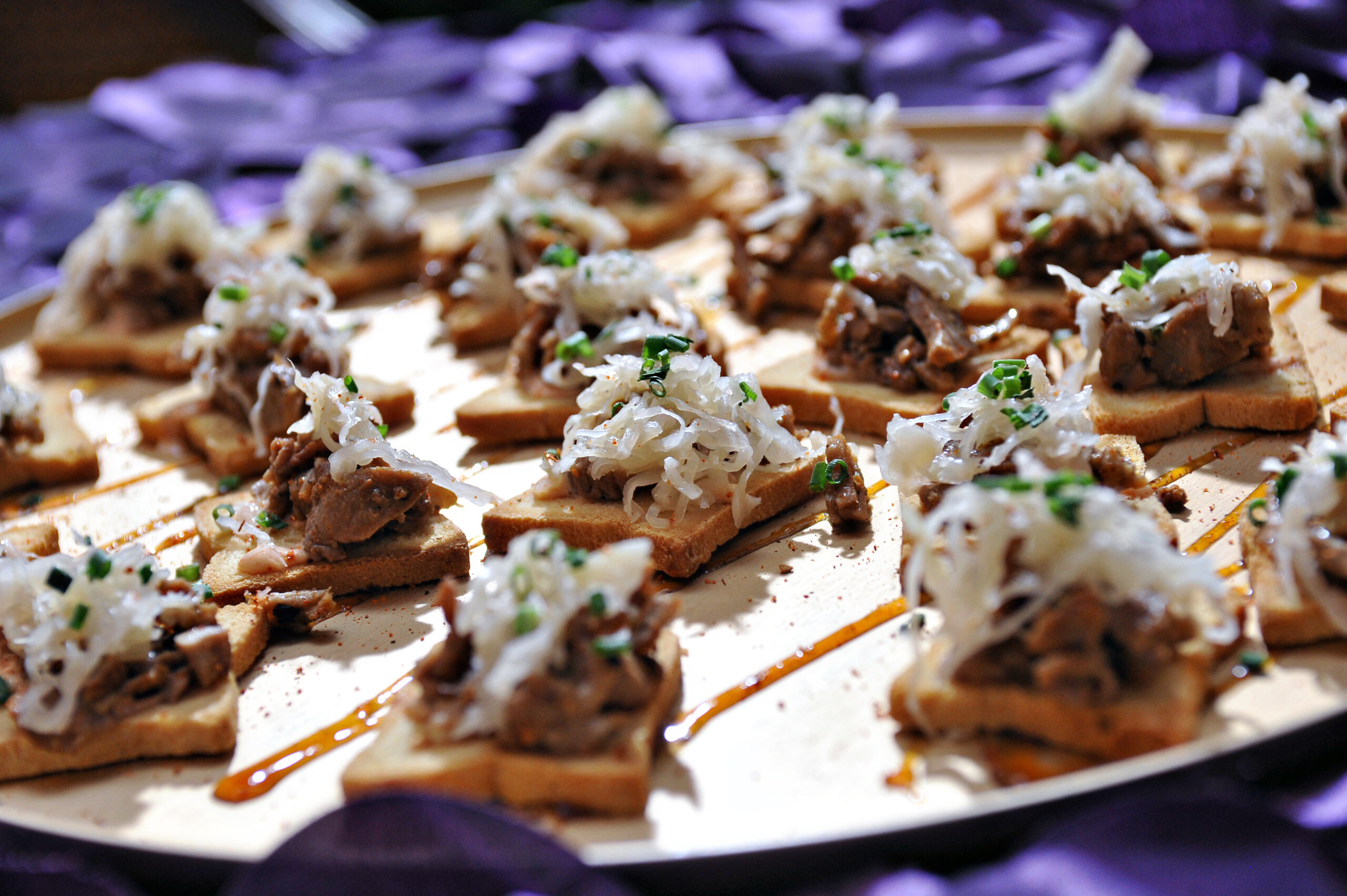 White ceramic spoons each holding a cooked shrimp on a small portion of sauce and garnished with green herbs, arranged on a black tray.