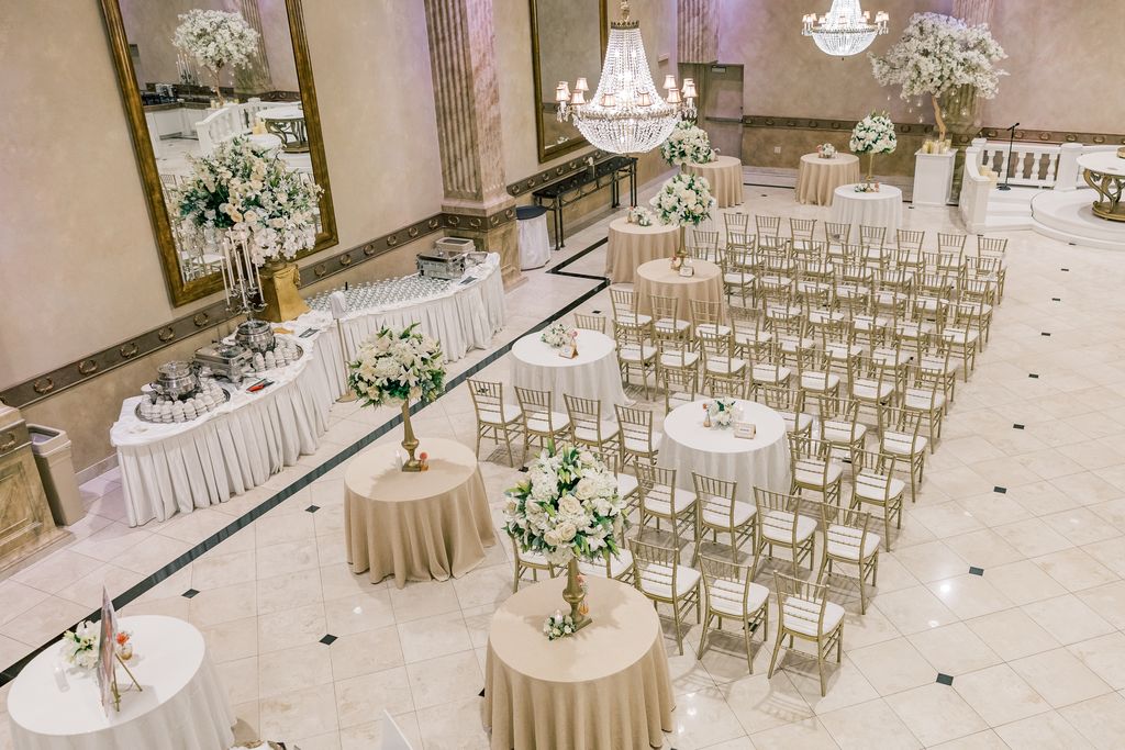 Large group of wedding guests smiling and waving around the bride and groom in a banquet hall.