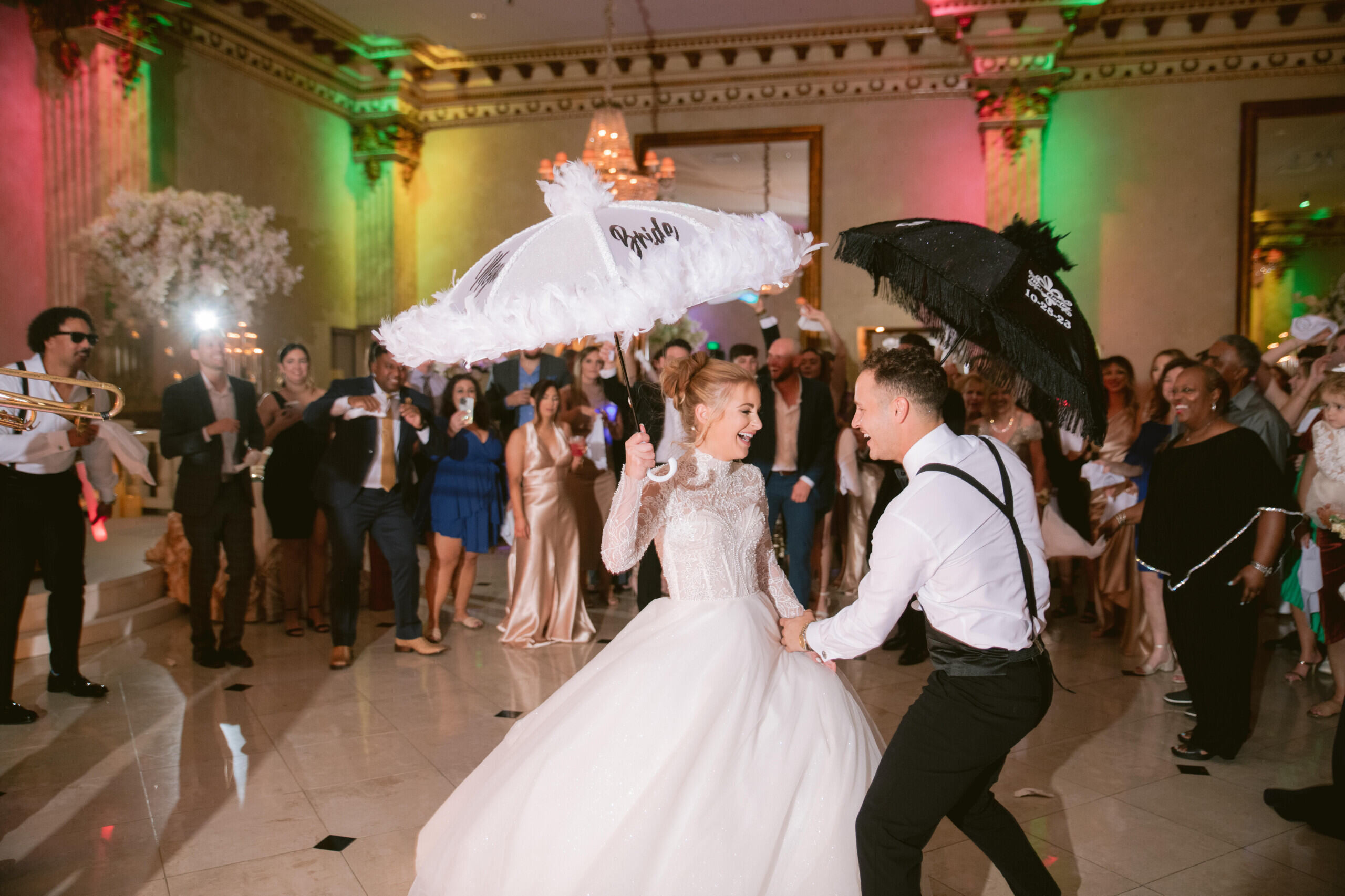 Bride and groom playfully feeding each other a hot dog under a yellow and red hot dog cart umbrella at night.