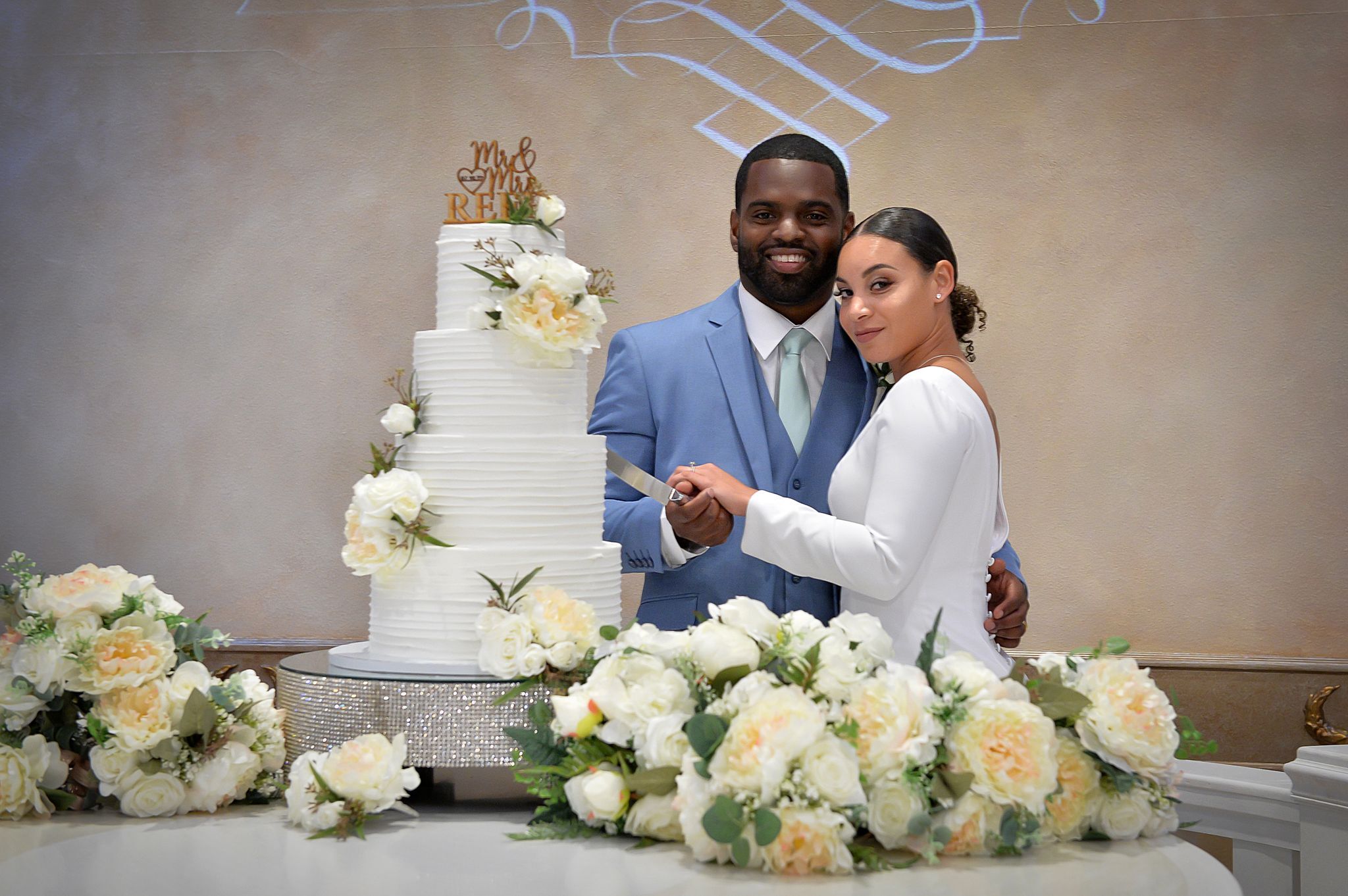 Bride in white dress with long train descending an indoor staircase with golden railings, smiling and holding the rail.