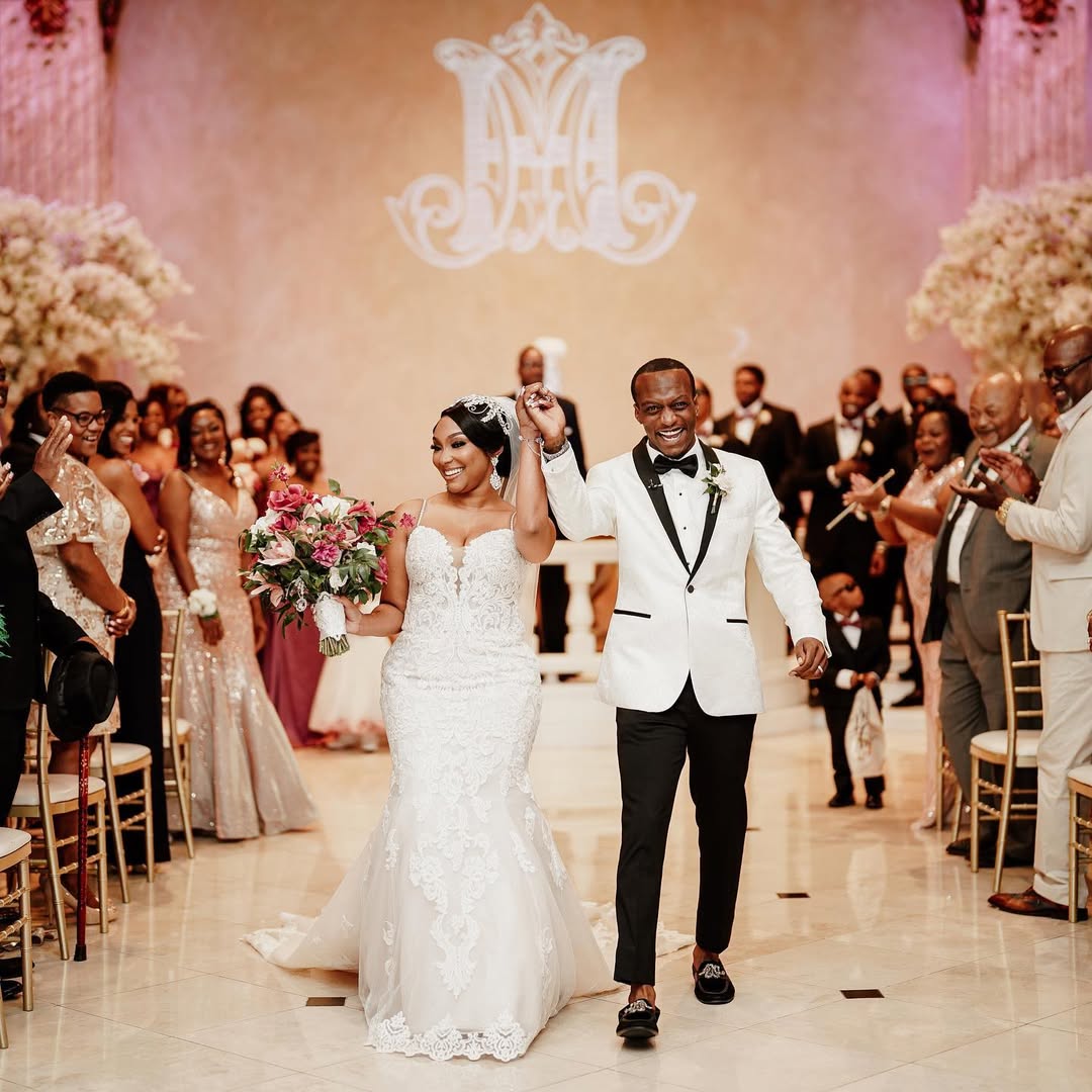 Groom in a white tuxedo looking emotional with hands clasped, standing in front of groomsmen in black suits with orange boutonnieres.