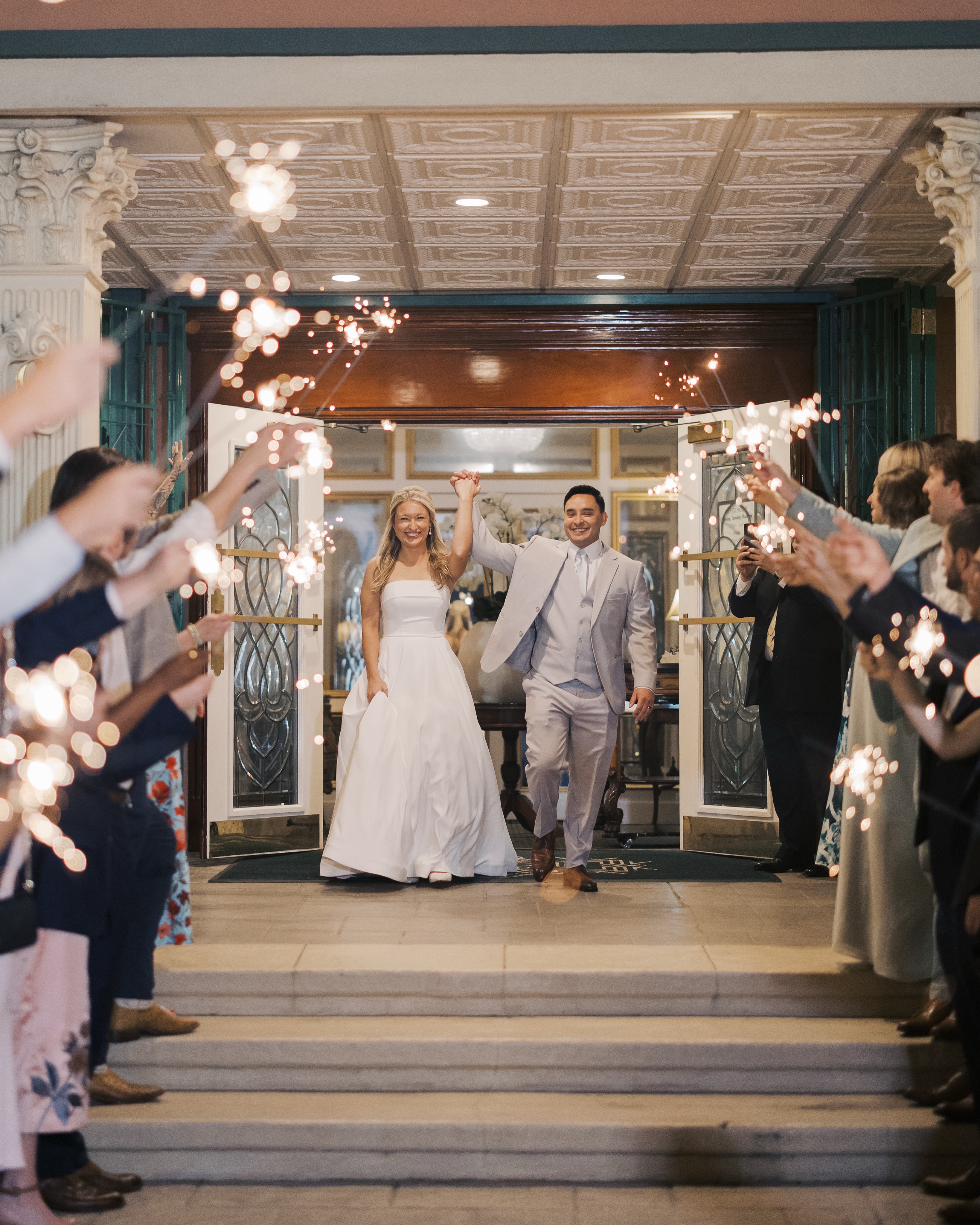 Bride in white dress with long train descending an indoor staircase with golden railings, smiling and holding the rail.