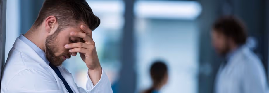 Young professional man in white shirt stressed with hand covering his face, blurred people in background.
