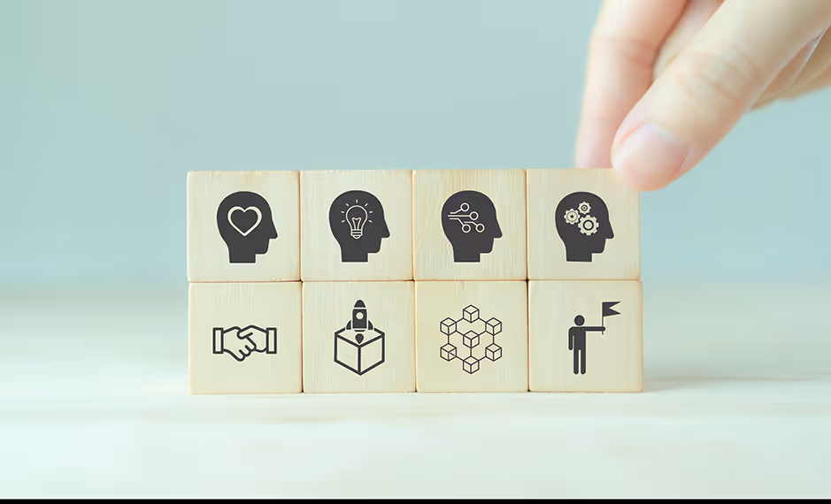 Hand placing wooden block with head and gears icon among blocks with various business and innovation icons.