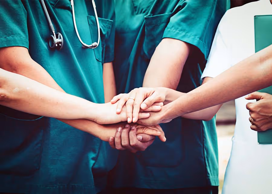 Healthcare professionals joining hands in a group showing teamwork and unity.