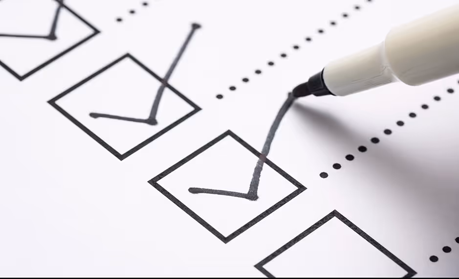 Black marker making a checkmark in a checkbox on a white checklist paper.