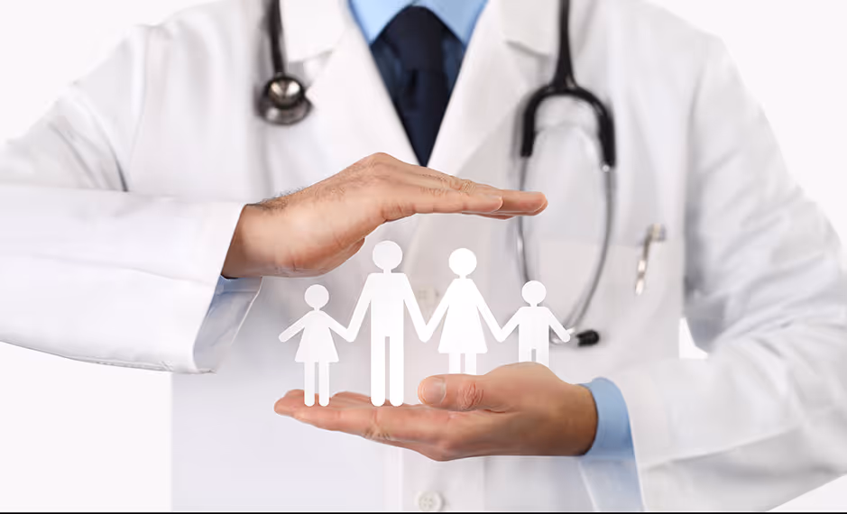 Doctor in white coat with stethoscope protecting a paper cutout of a family of four with hands.