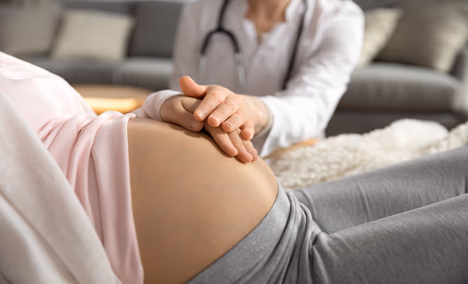 Doctor with stethoscope holding hands over a pregnant woman’s bare belly.