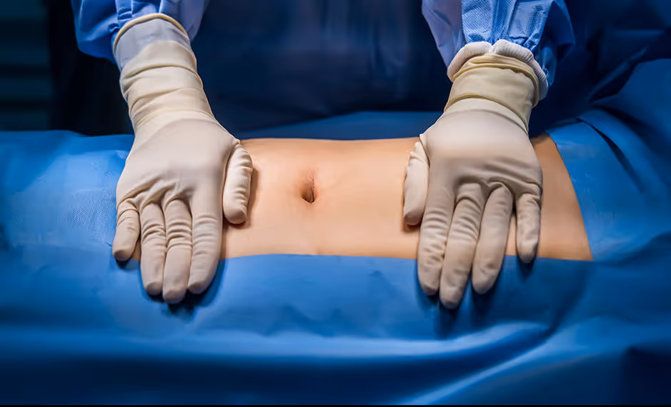 Hands in medical gloves palpating a patient's exposed abdomen during an examination.