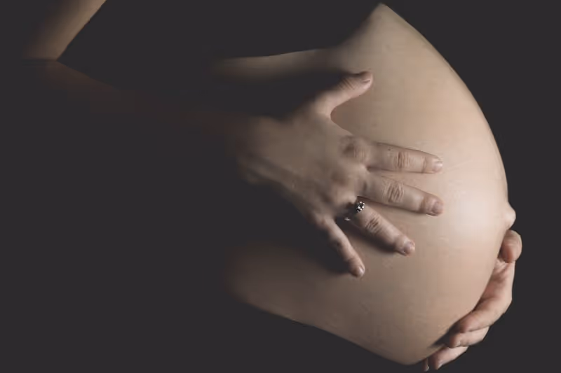Close-up of hands gently holding a pregnant belly against a dark background.