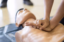 Hands performing chest compressions on a CPR training manikin during a first aid course.