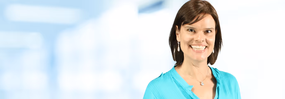 Smiling woman with short brown hair wearing a turquoise blouse and earrings on a light background.