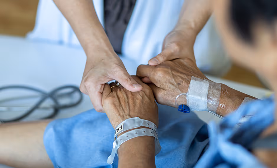 Close-up of a caregiver holding a patient's hands with a hospital wristband and IV line.