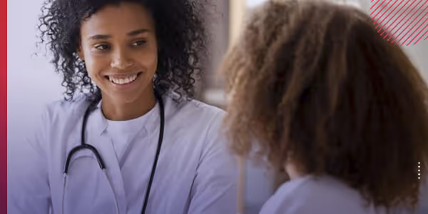 Female doctor with a stethoscope smiling and talking to a patient with curly hair.