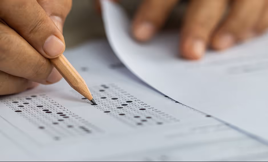 Hand holding a pencil filling out multiple-choice answer sheet on a test or exam paper.