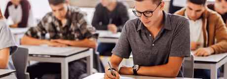 Students sitting at desks writing in a classroom during an exam or test.