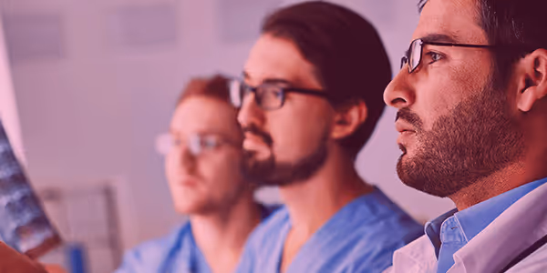 Three focused medical professionals examining an X-ray image in a clinical setting.