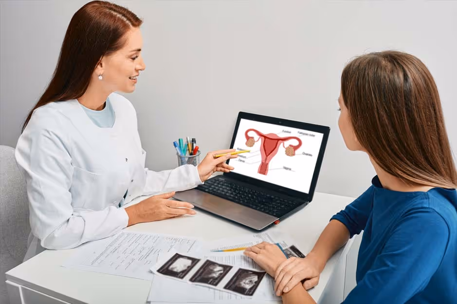 Doctor explains female reproductive system on laptop to woman holding ultrasound images.
