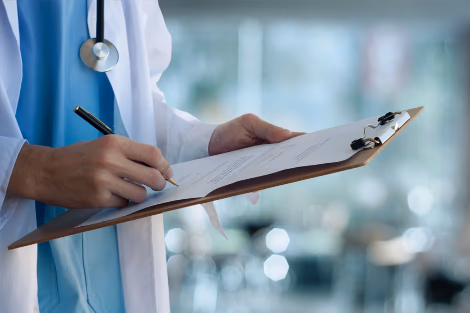 Doctor in white coat writing on a clipboard with a stethoscope around the neck.