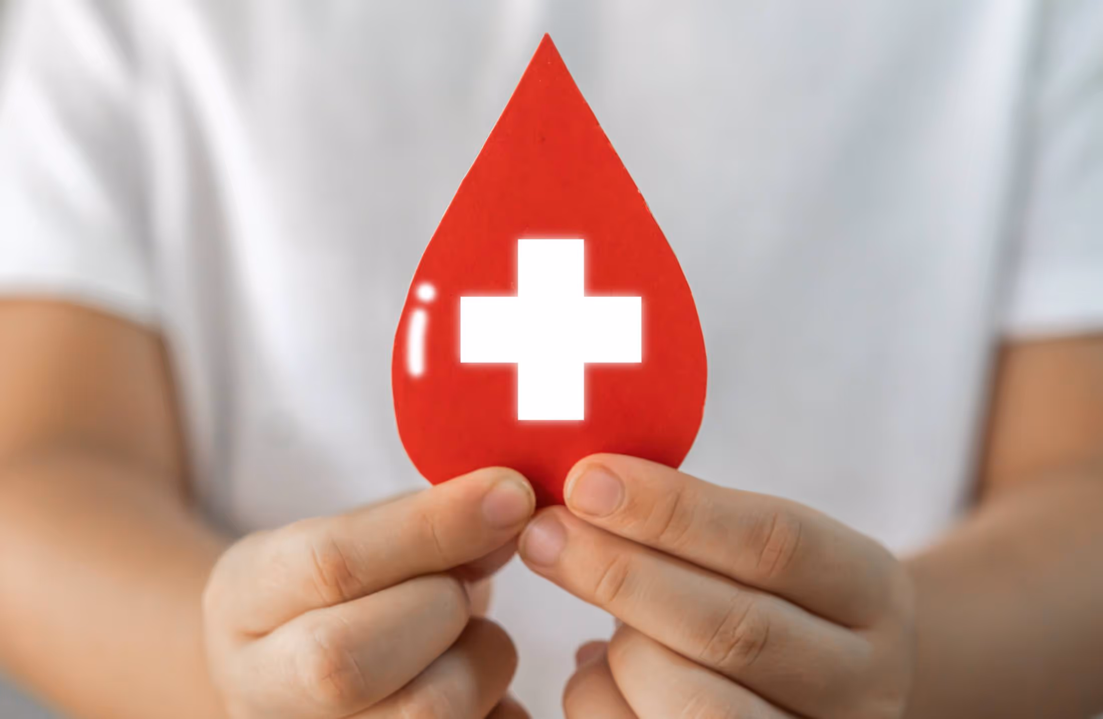 Person holding a red paper cutout shaped like a blood drop with a white medical cross inside.