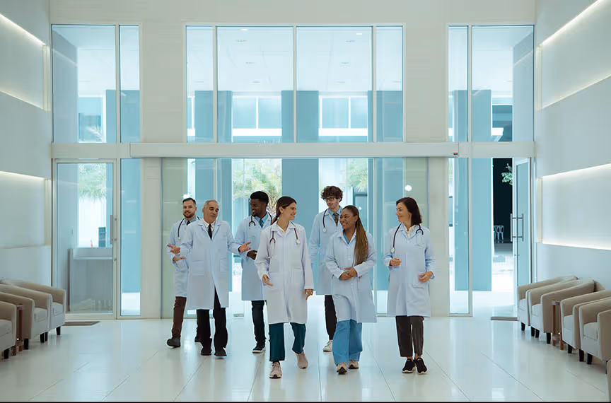 Group of diverse doctors in white coats walking and talking inside a bright hospital lobby.