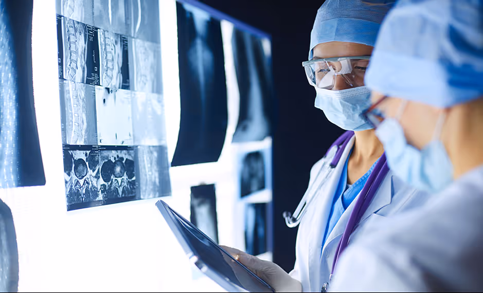 Two medical professionals reviewing X-ray images on a lightbox in a clinical setting.