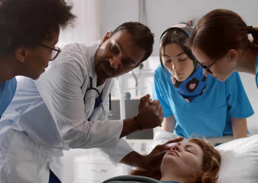 Doctor explaining to medical students while examining a woman patient lying in a hospital bed.
