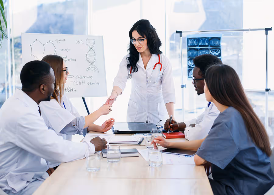 Female doctor shaking hands with colleague during medical team meeting in a bright conference room.