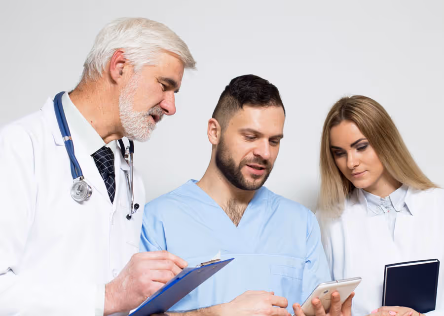 Three healthcare professionals reviewing information on a clipboard and smartphone together.