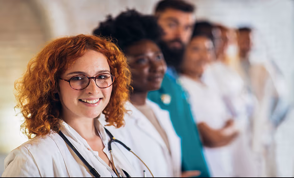 Smiling diverse medical team standing in a line with the closest woman wearing glasses and a stethoscope.