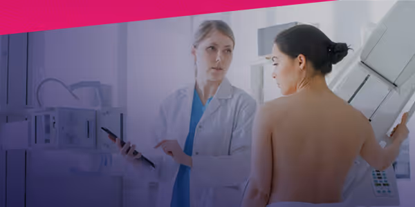Female doctor holding a tablet talks with a woman at a mammography machine during a breast exam.