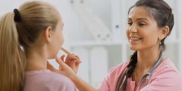Medical professional examining a patient's throat with a tongue depressor in a clinical setting.