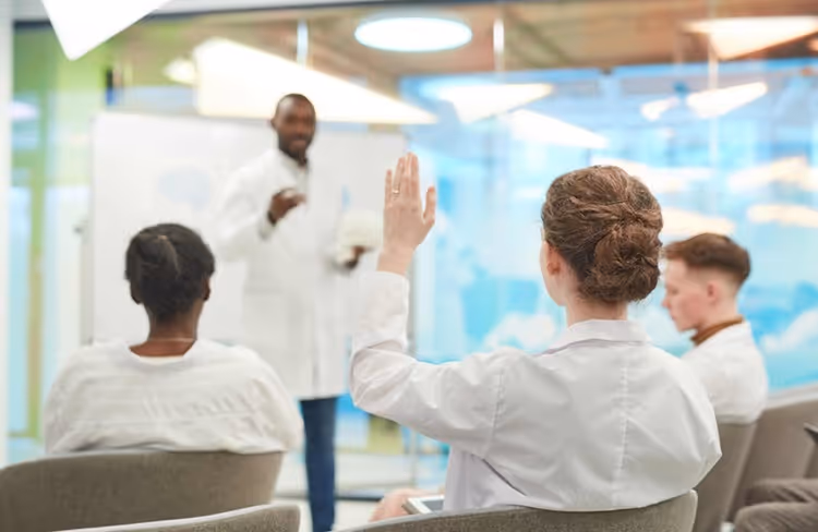 Medical professional raising hand during a discussion with colleagues in a conference room.