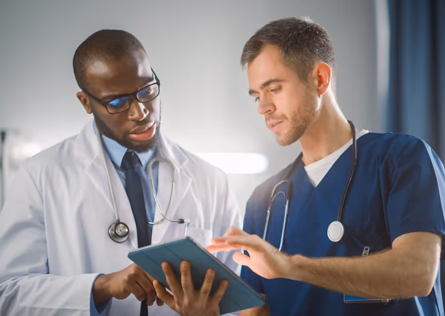 Two male doctors in scrubs and lab coat reviewing information on a digital tablet together.