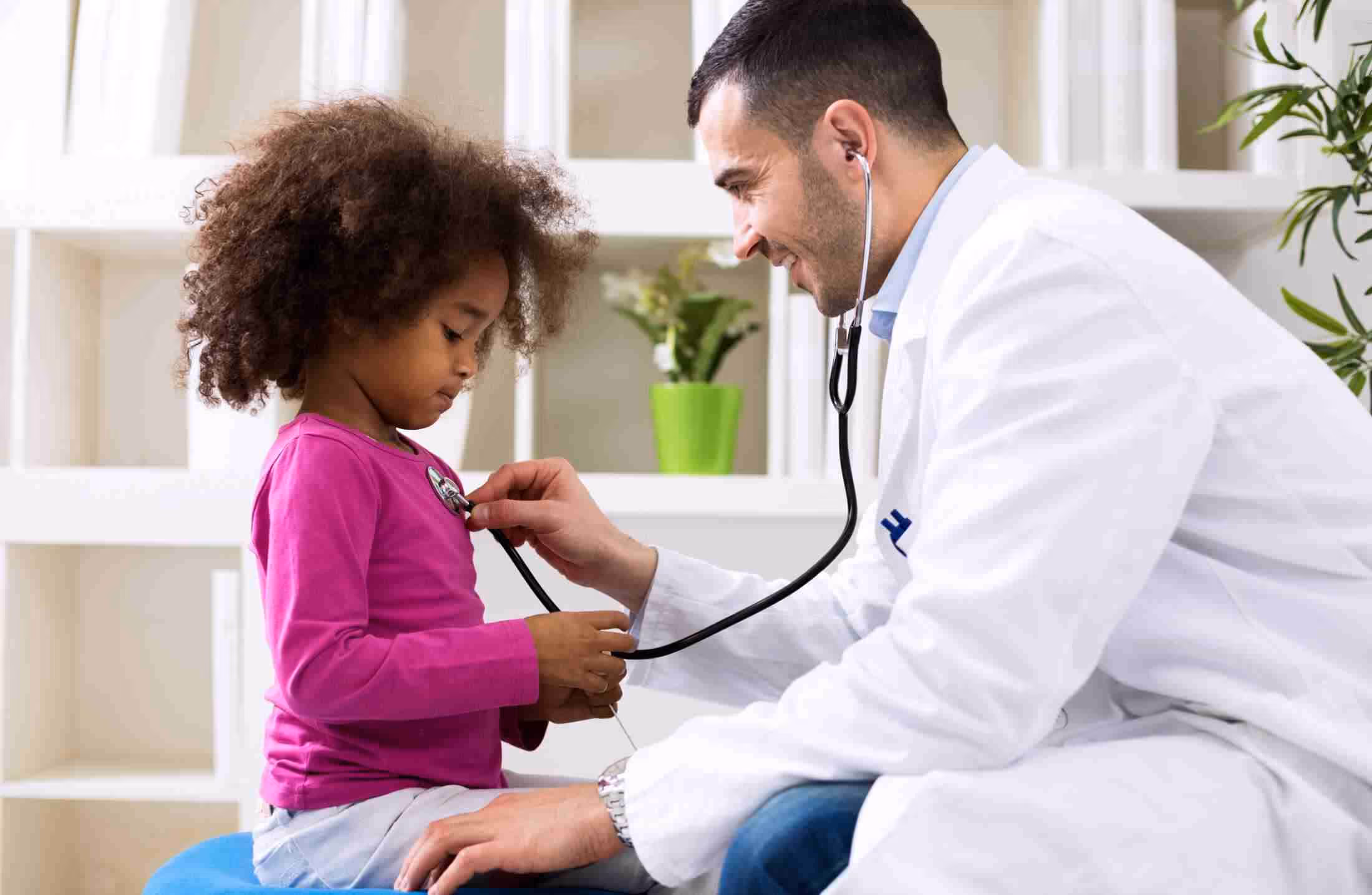 Doctor using a stethoscope to examine a young girl in a bright medical office.