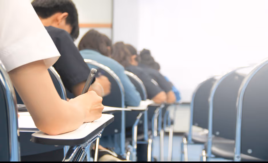 Students seated in rows writing on desks in a classroom or exam setting.