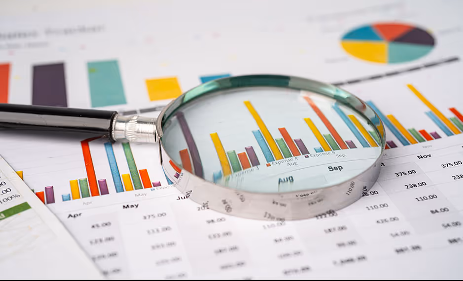 Magnifying glass over colorful bar charts and data tables on printed financial reports.