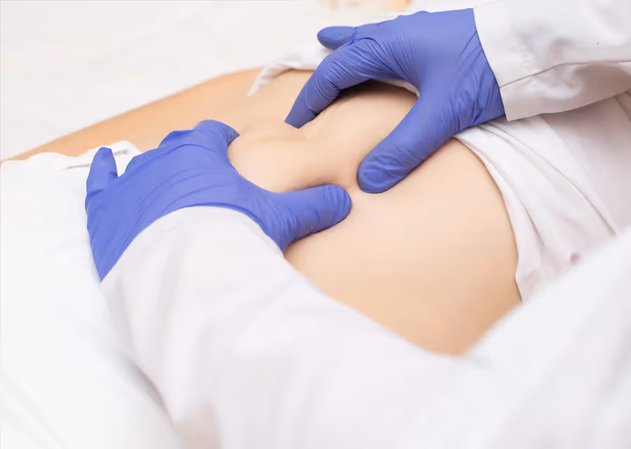 Doctor wearing blue gloves pressing on a patient's abdomen during a medical exam.