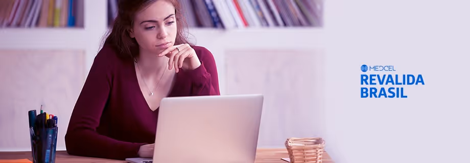 Young woman with dark hair in a burgundy sweater intently looking at a laptop in a room with bookshelves.