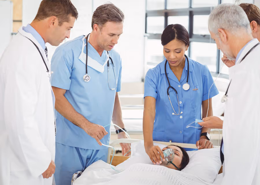 Medical team of doctors and nurse attending a patient lying in a hospital bed with oxygen mask.