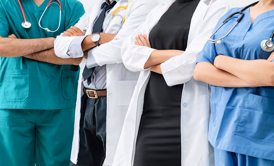 Four healthcare professionals standing side by side with arms crossed, wearing scrubs and lab coats.