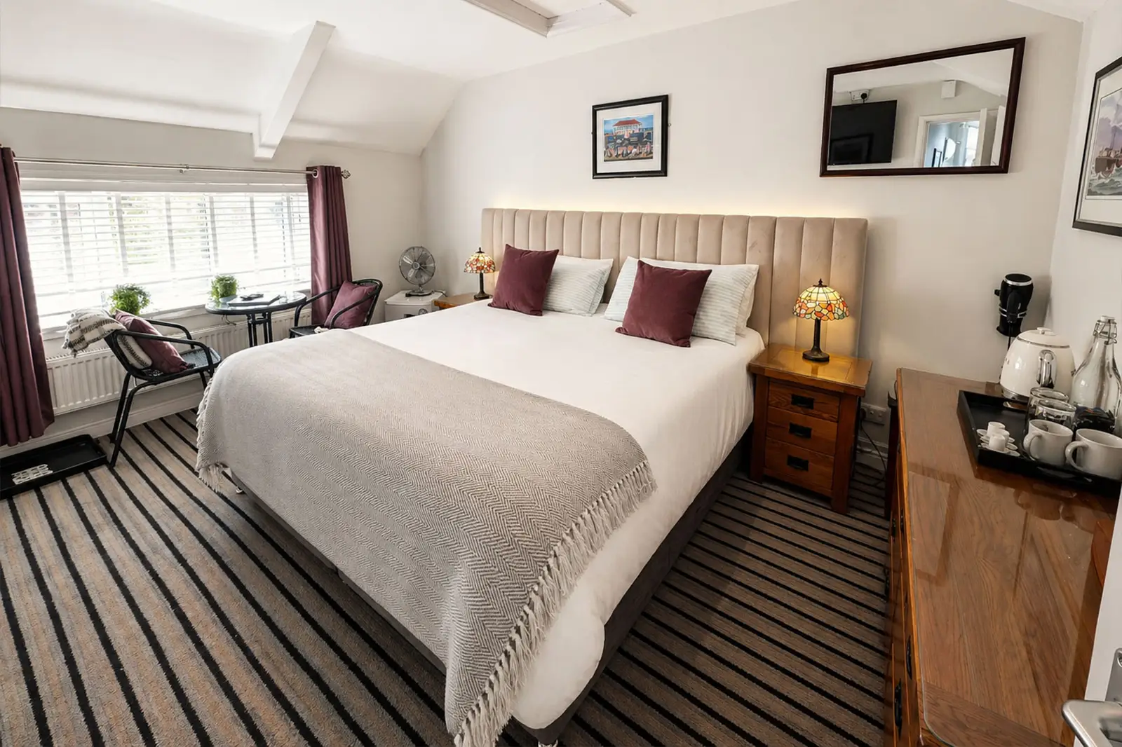 A large double bedroom with double bed featuring white sheets, red pillows and a Tiffany lamp on either side
