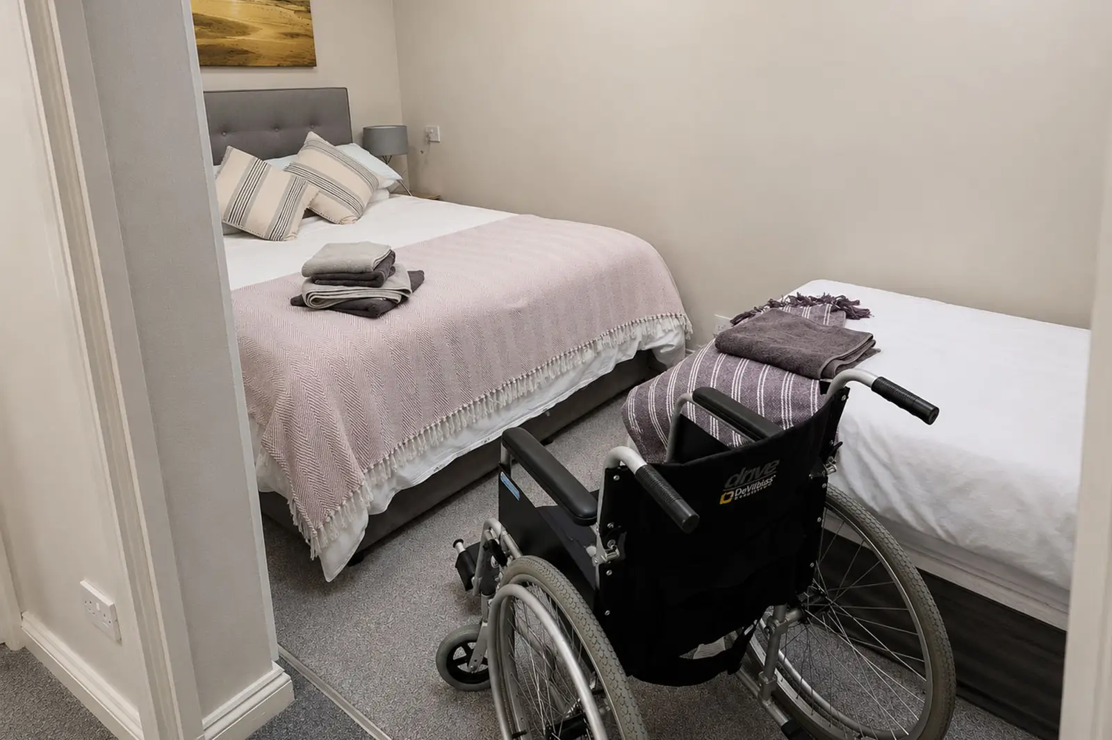 A small room with twin and single beds and a wheelchair showing accessibility to the bedroom with a wheelchair